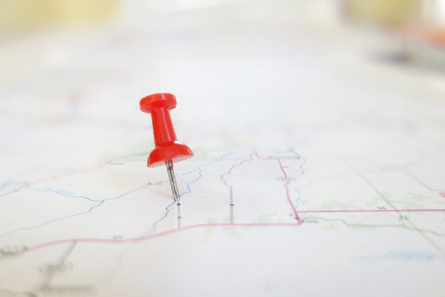 Karte aus Papier liegt auf einem Tisch und eine rote Pin-Nadel markiert einen Standort