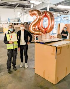 Mitarbeiterin steht neben der Geschäftsführerin bekommt zum 10-jährigen Firmenjubiläum eine Urkunde und Helium-Ballons in Form einer 20