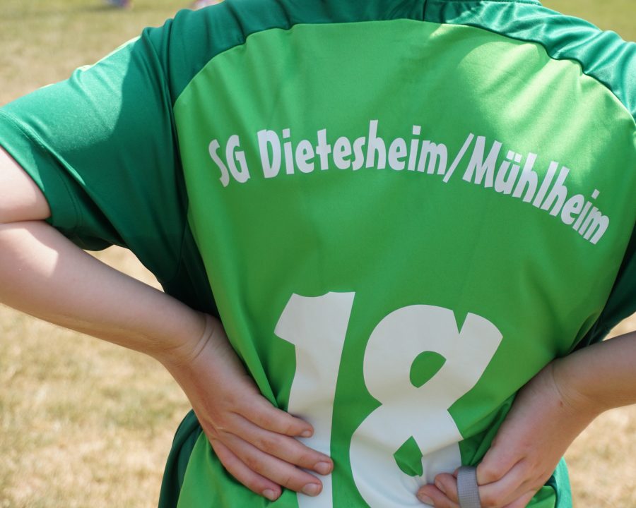 Nahaufnahme eines grünen Trikots von SG Dietesheim/Mühlheim von hinten. Das Trikot wird von einem Kind getragen. Der Schriftzug befindet sich oberhalb der mittig ausgerichten Zahl 18.